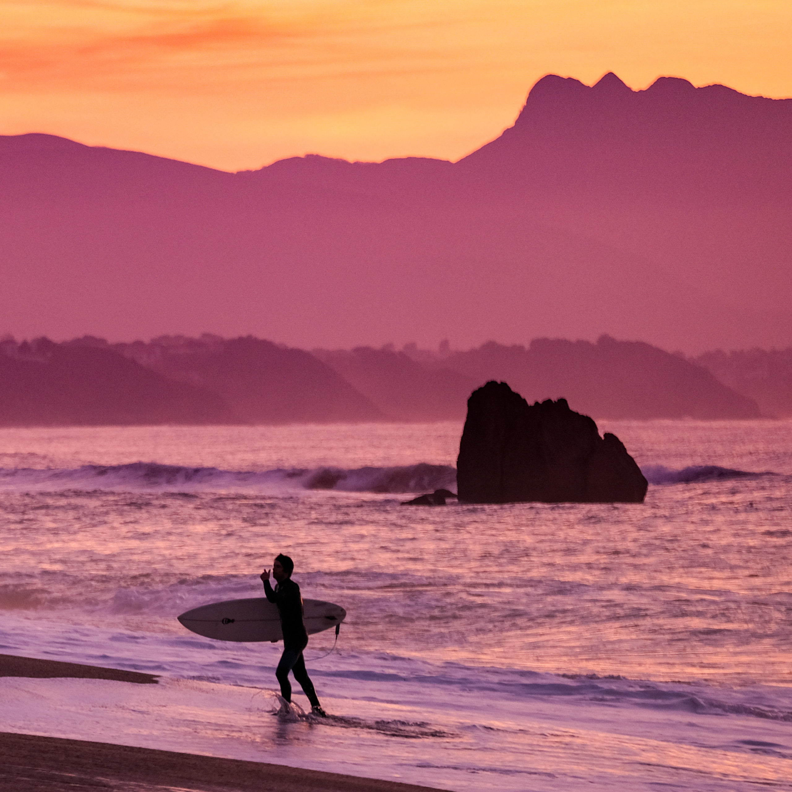 Un surfeur sort de l'océan pendant le coucher de soleil